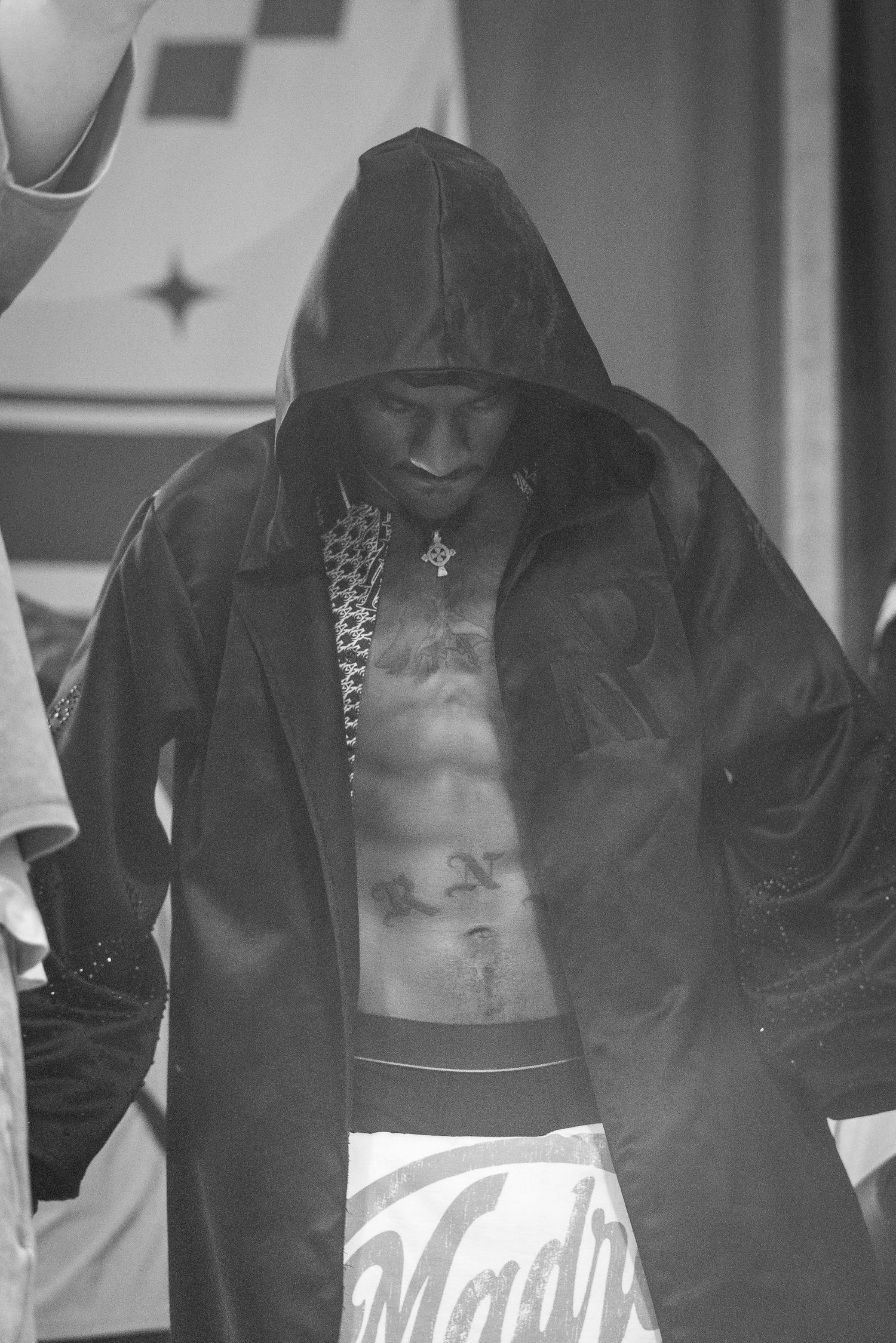 A black-and-white photo of a hooded boxer with tattoos looking down in a satin robe and trunks reading Madrid.