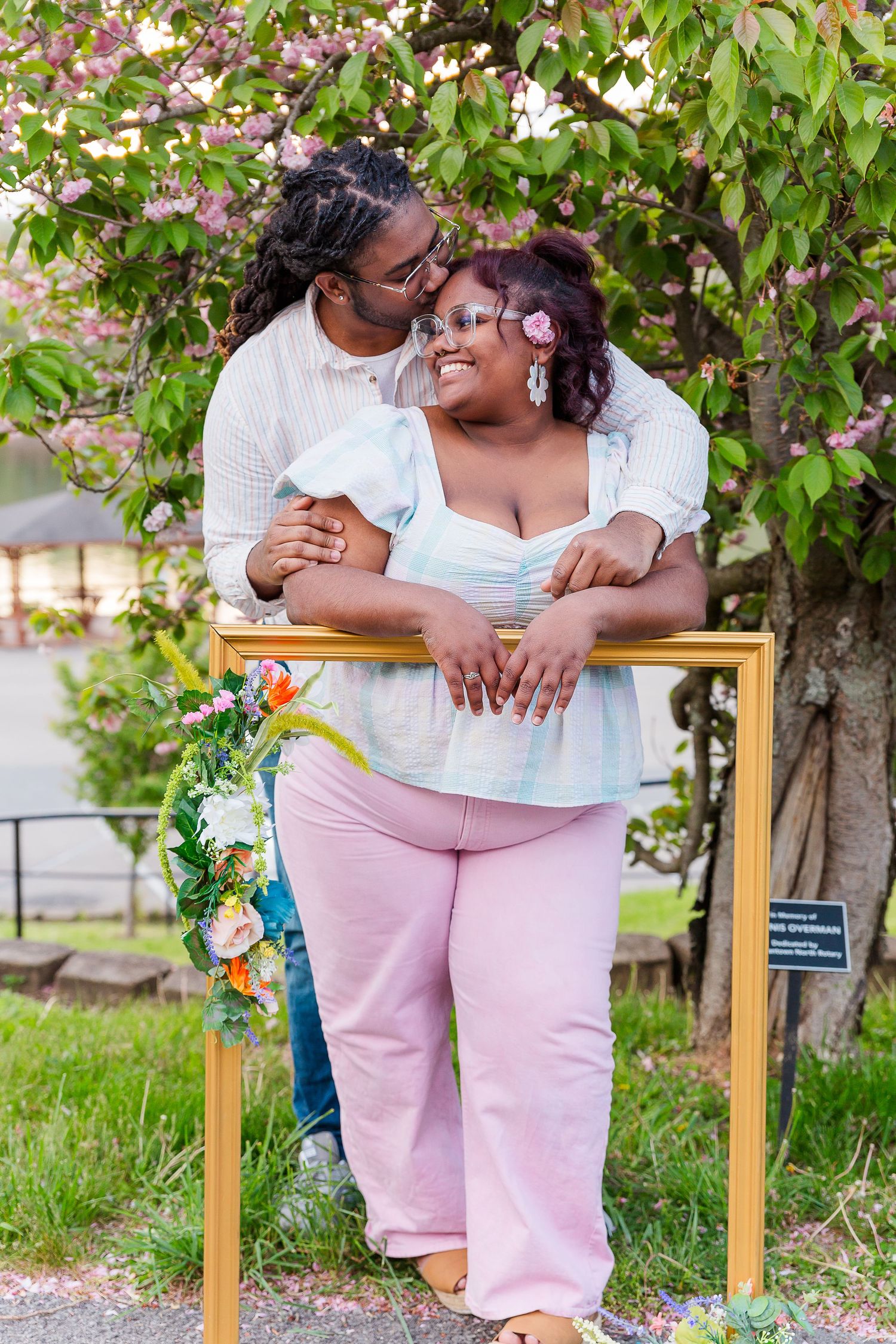 Couple shares intimate moment on bench surrounded by spring blossoms.