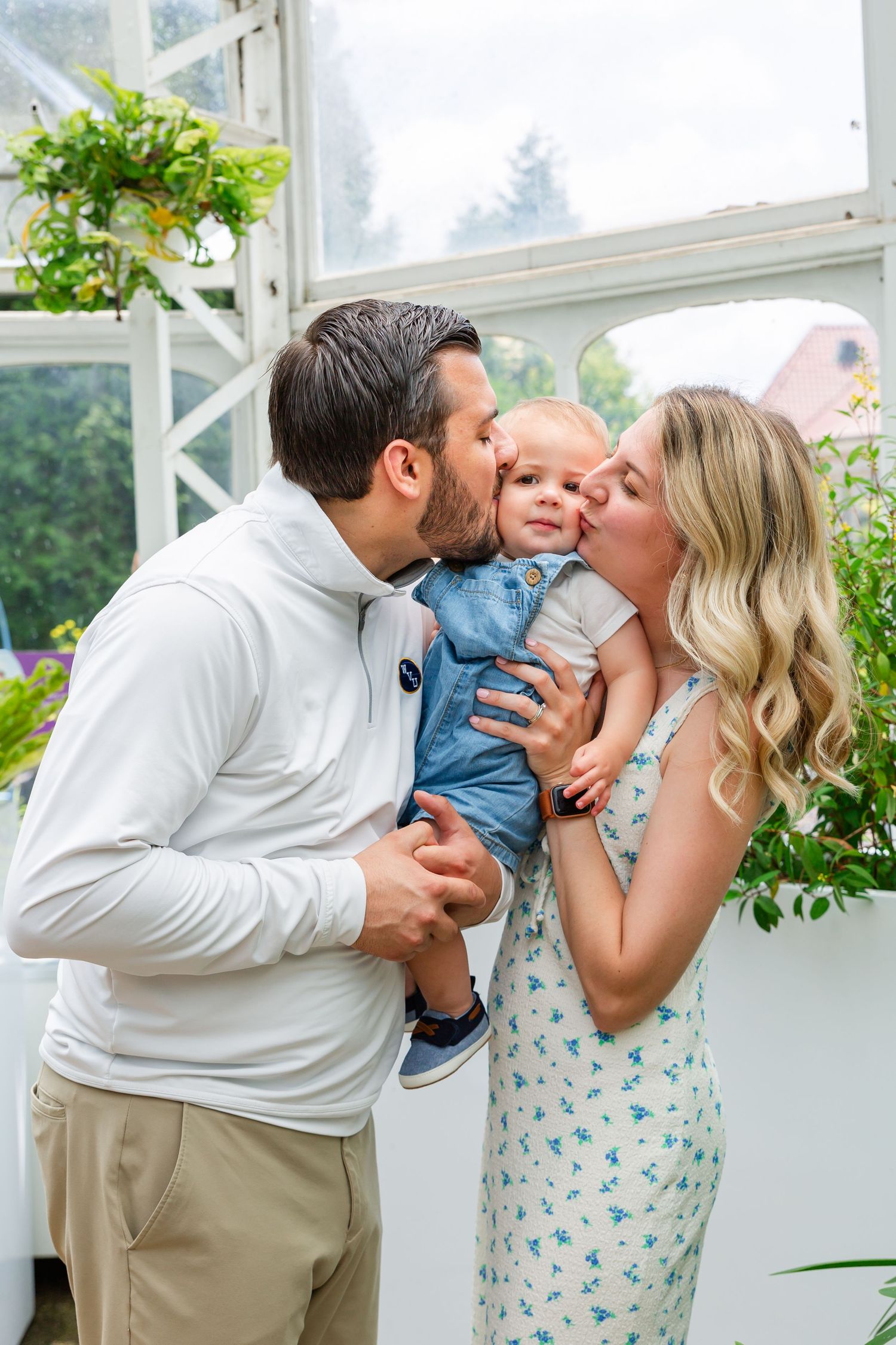 A tender family moment captured in a bright greenhouse setting with plants.