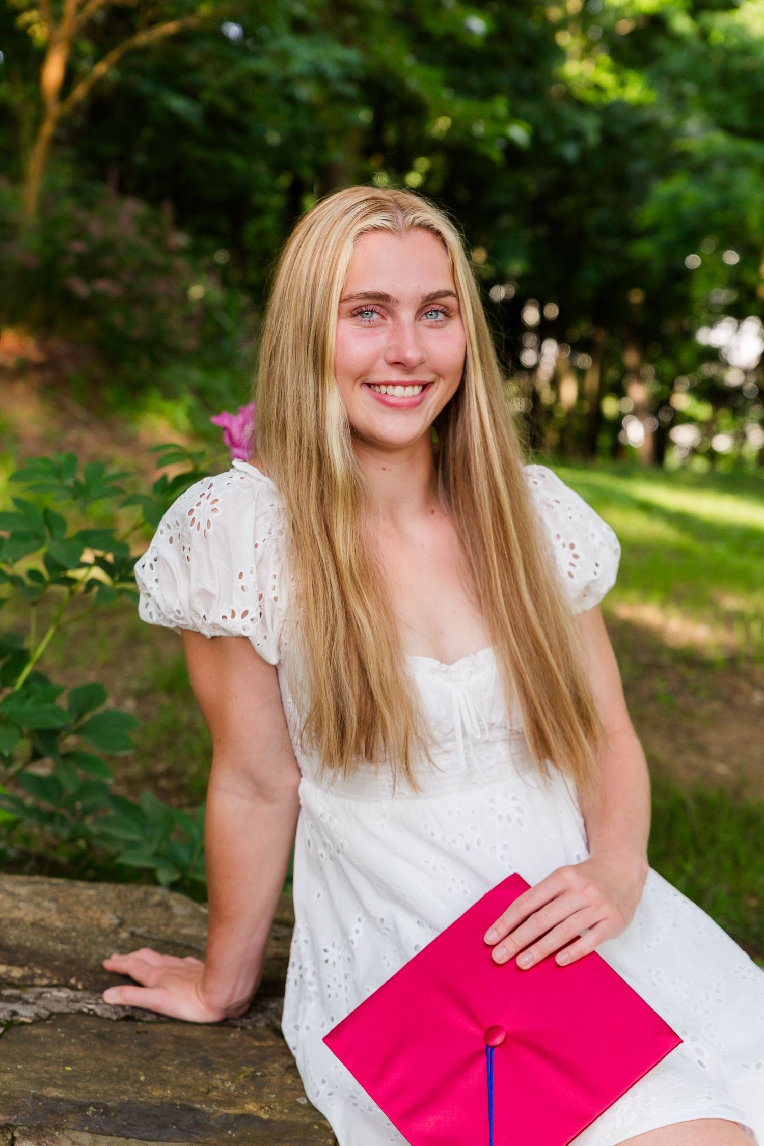 White eyelet dress portrait with pink graduation diploma on stone wall background.
