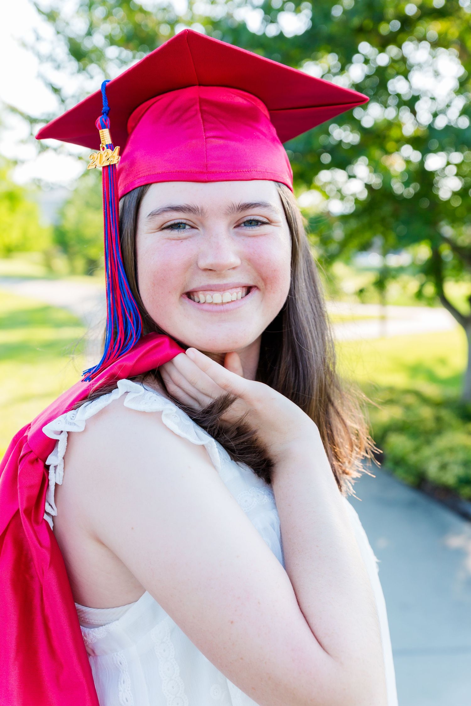 Graduate in red cap and gown poses for celebratory portraits outdoors.