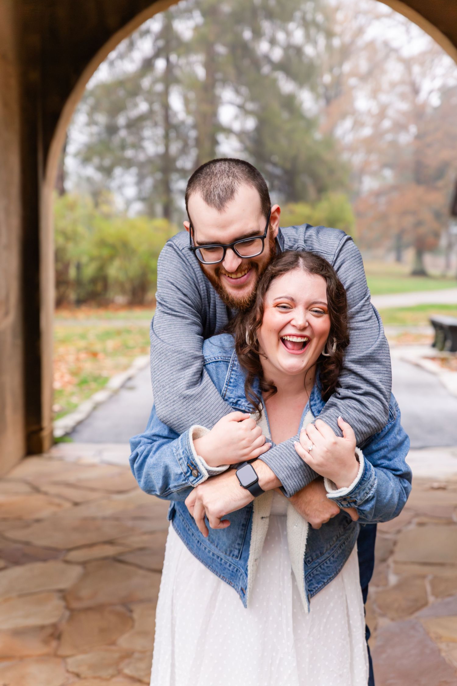 A playful embrace captured under a stone archway on a fall day.
