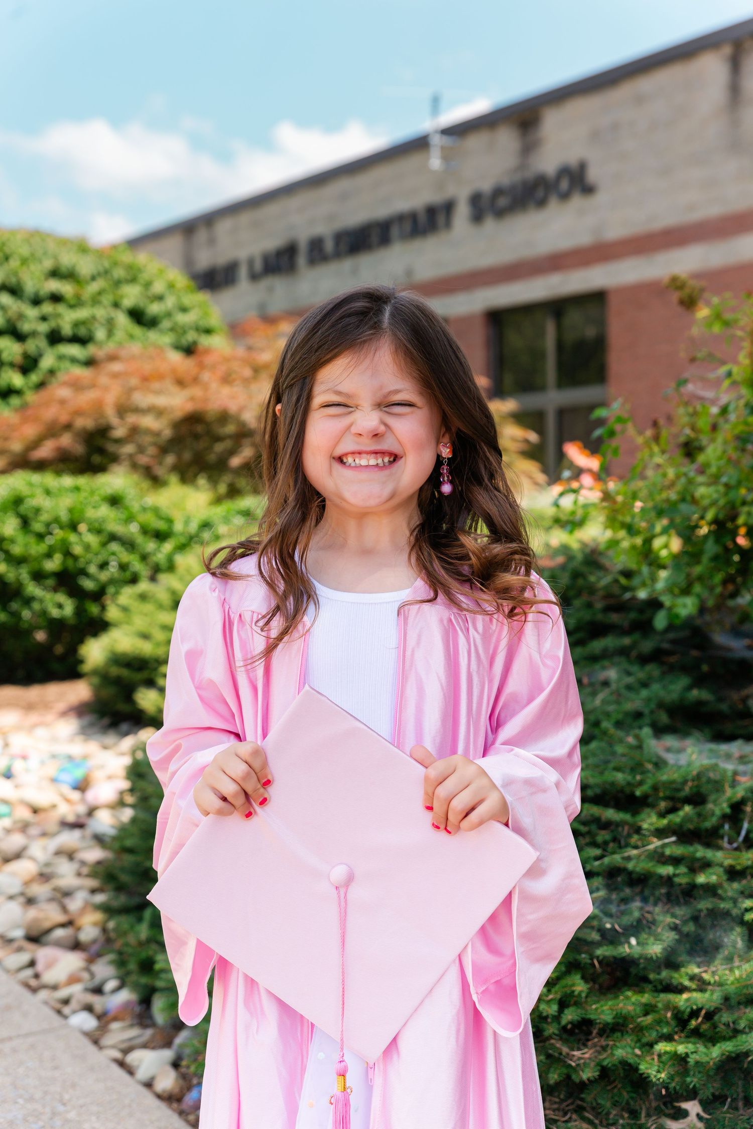 Pink graduation robes stand out against brick school building in celebratory photos.