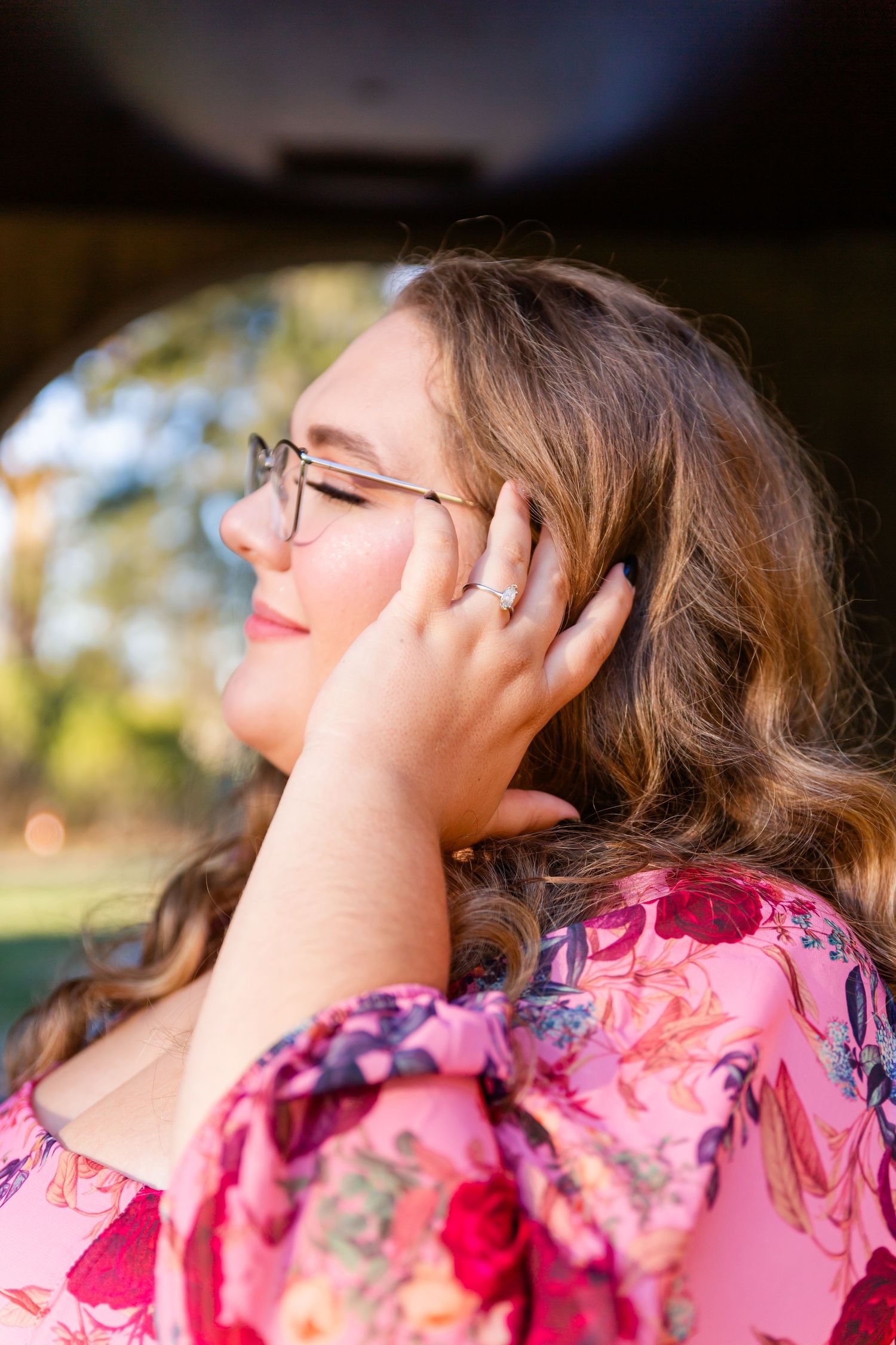 A person in a pink floral top leans back with eyes closed in a natural outdoor setting during golden hour.