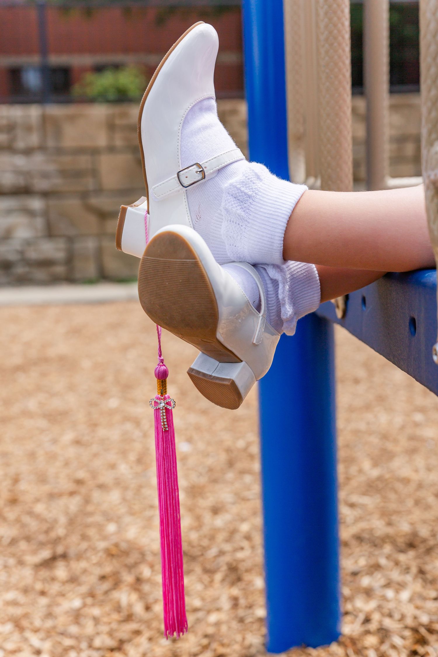 Pink graduation tassels dangle from white shoes against a playground background.