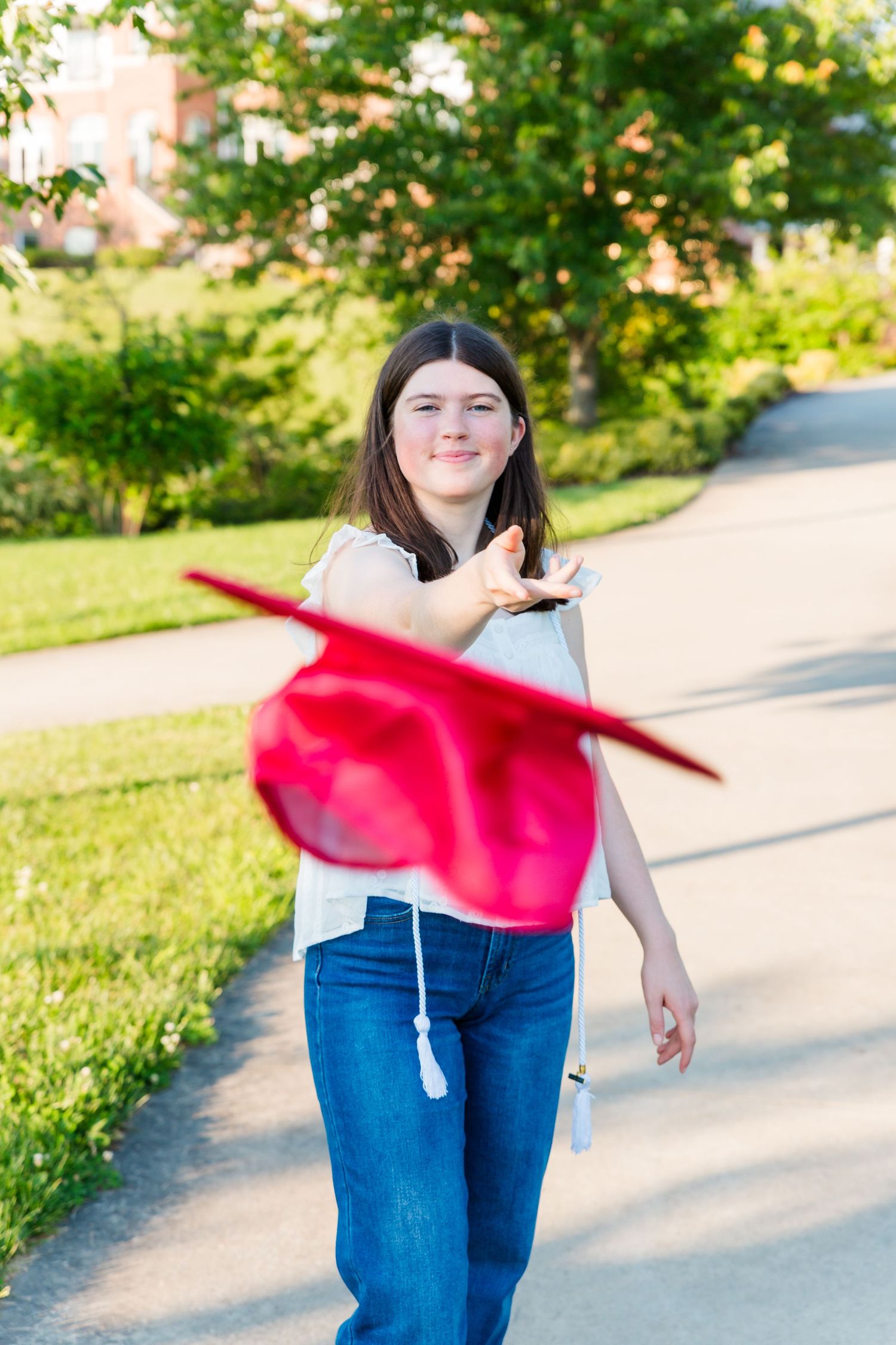 Happy graduate tossing red graduation cap in the air outdoors on a sunny day.
