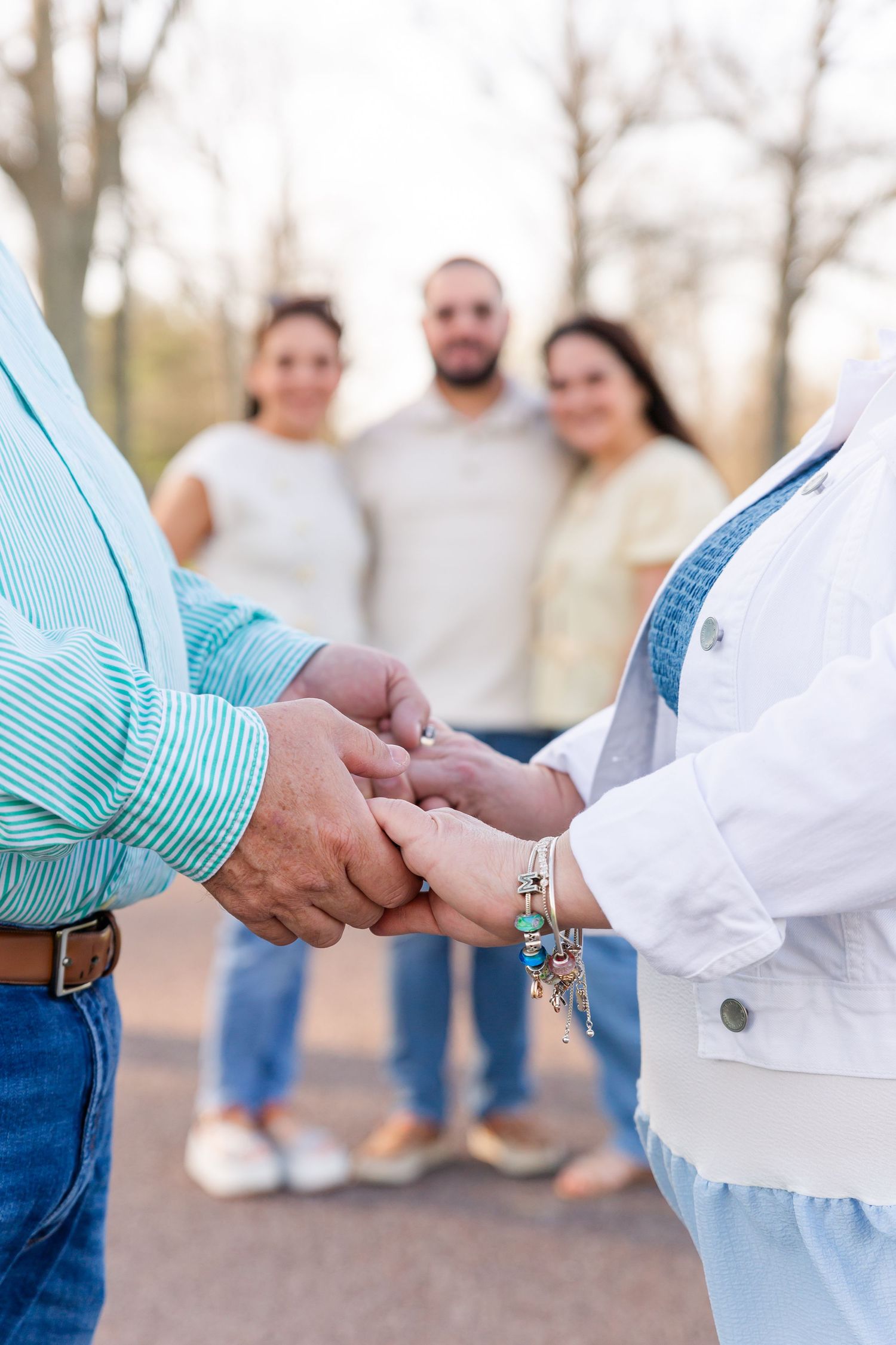 Close up of hands clasped together with people standing in background outdoors.