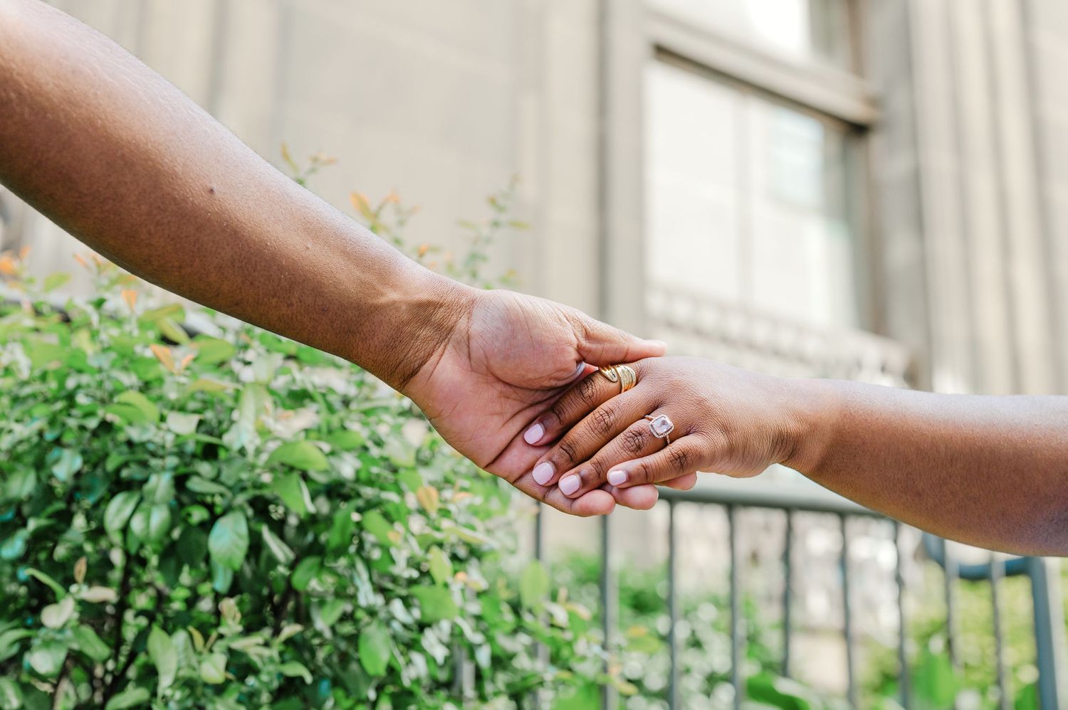 Two people of different ethnicities holding hands outdoors near green bushes, symbolizing unity and connection.
