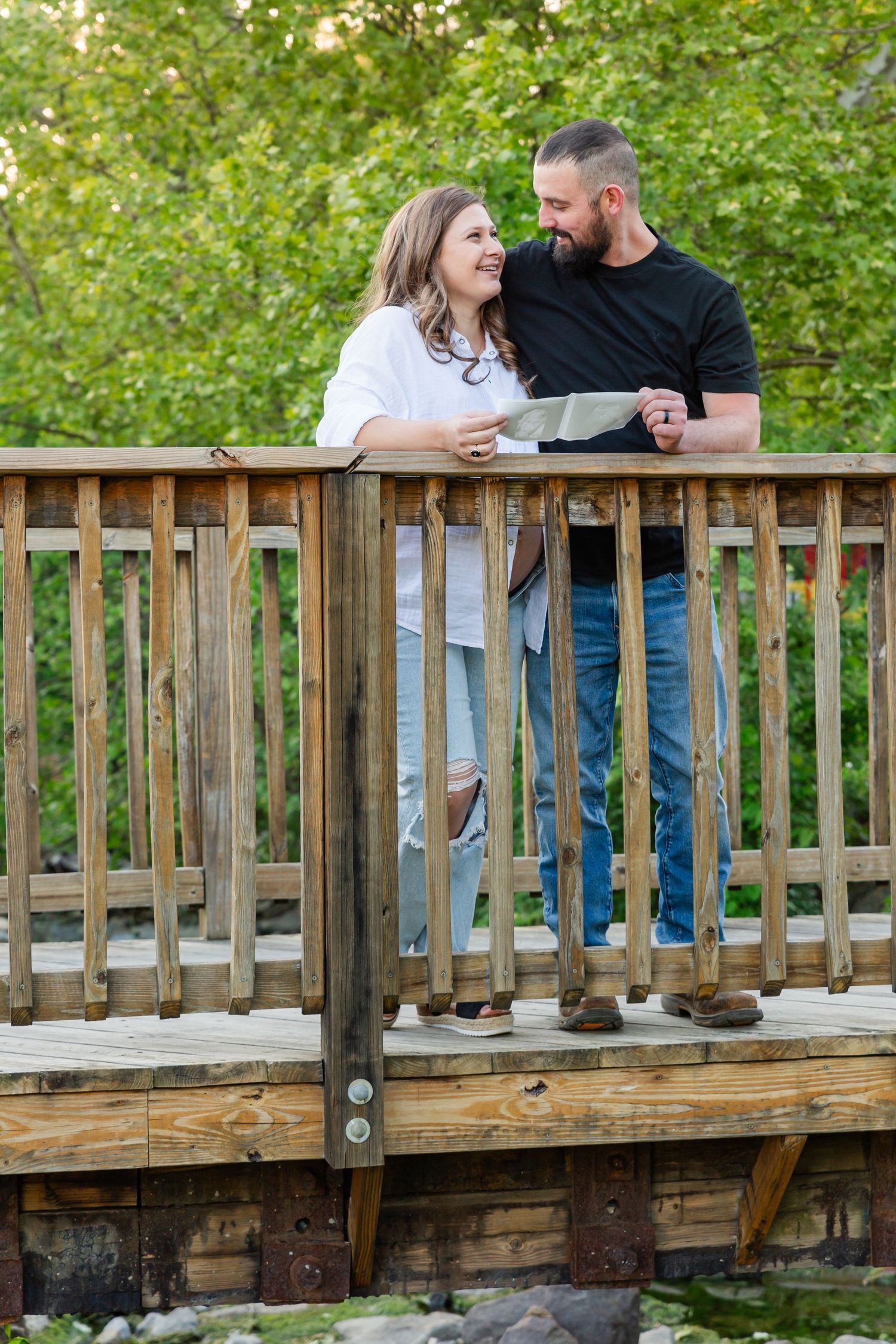 A couple shares a romantic moment on a wooden bridge surrounded by greenery.