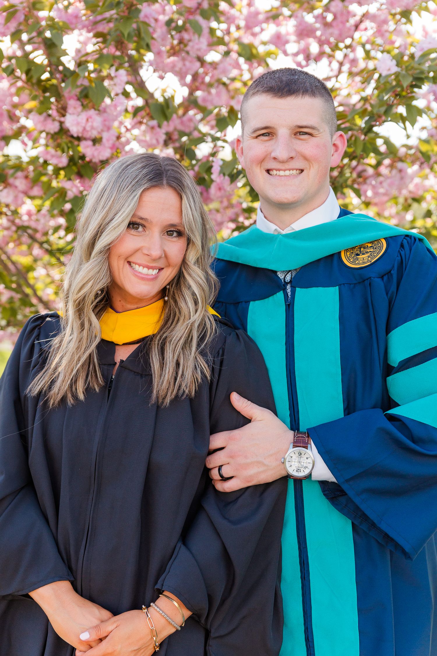 Graduation photos with academic regalia against blooming pink cherry blossoms.
