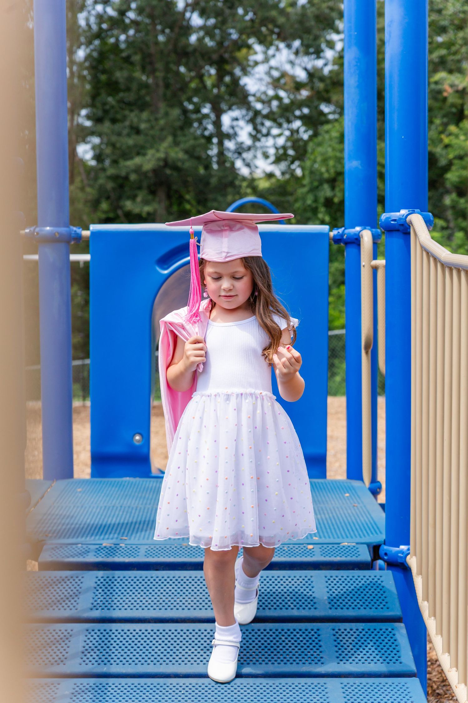 A white dress and pink graduation gown create movement on a blue playground bridge.