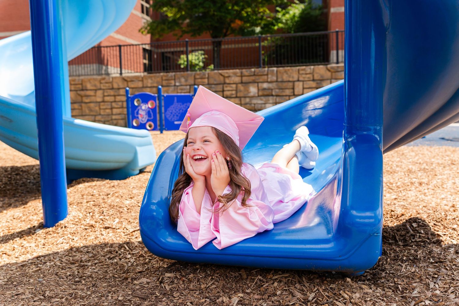 Pink-robed figure sliding down blue playground slide with joyful expression.