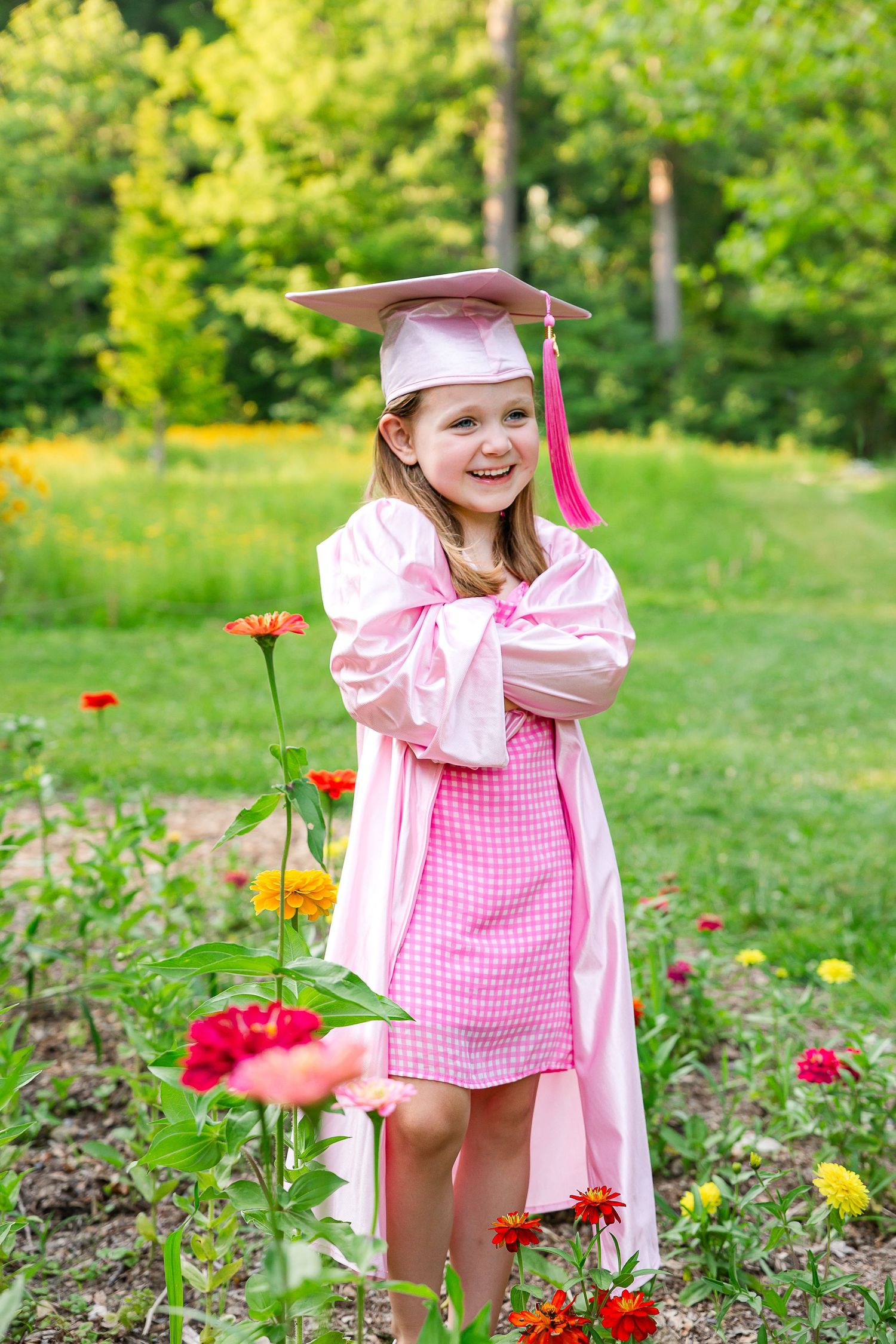 Child playing among colorful flowers wearing pink dress and graduation cap.