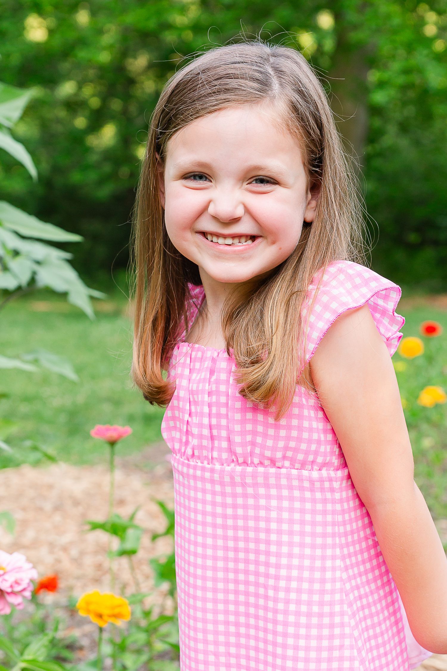 Young person wearing pink gingham dress smiling in garden setting.