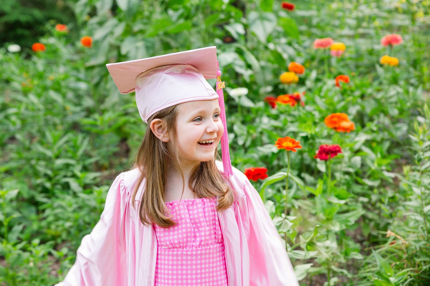 Child in pink gingham dress playing in garden with colorful flowers.