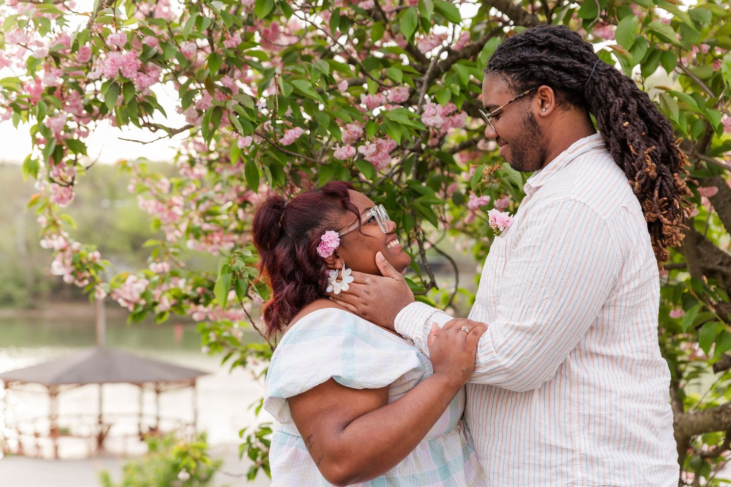 A romantic couple embraces under pink flowering trees during a spring photoshoot.