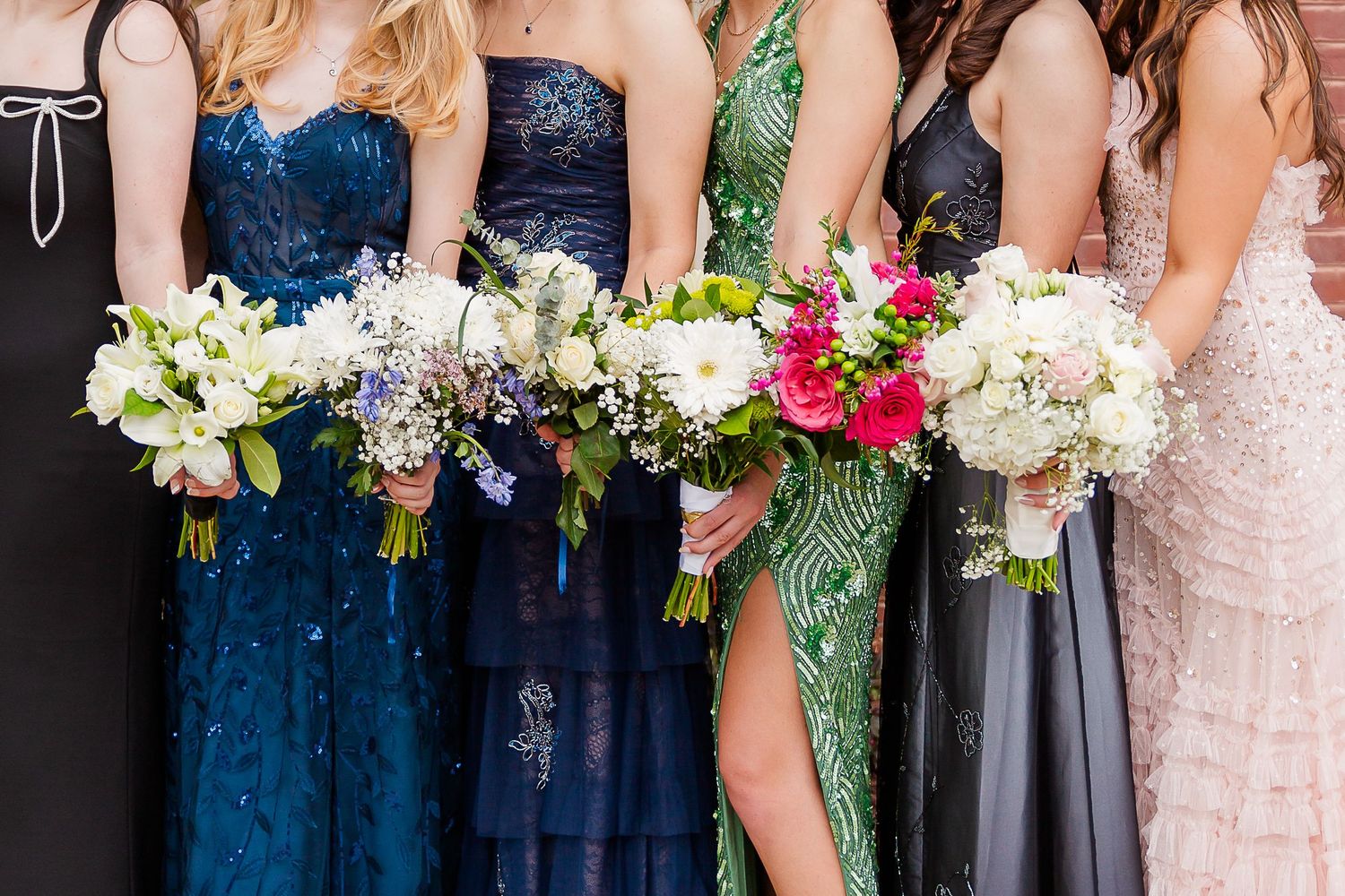 Bridesmaids in navy, green, and black sequin gowns holding white and pink floral bouquets at a wedding.