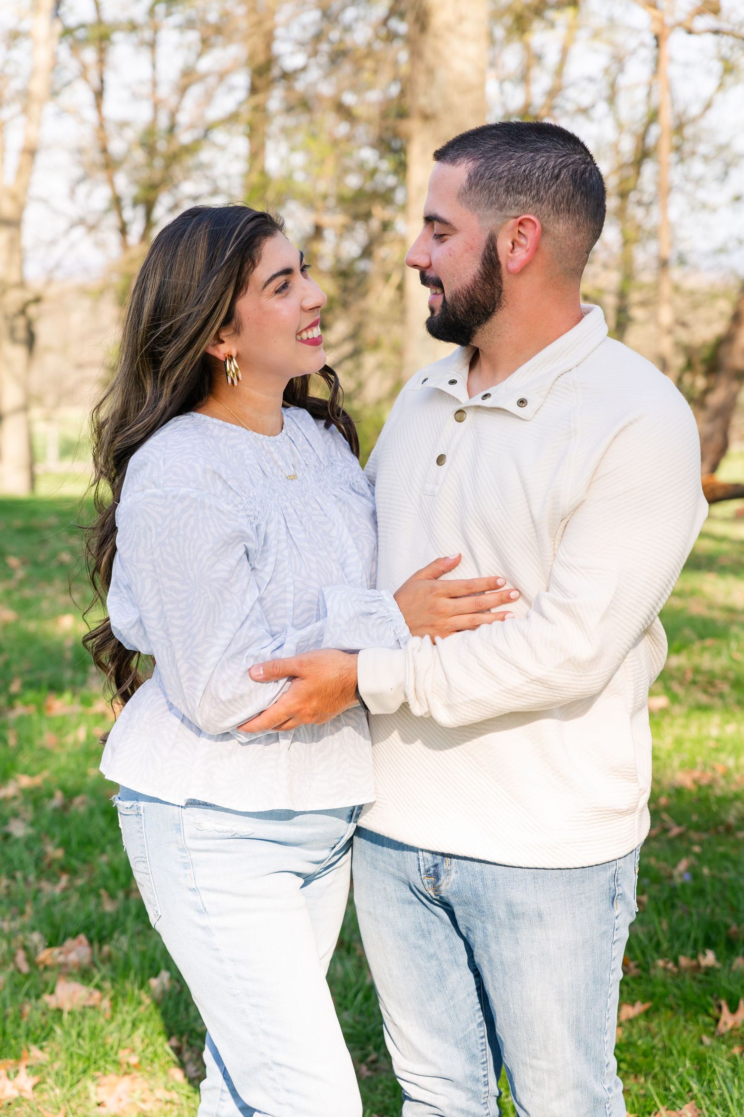 A couple in matching light-colored outfits share an intimate moment in an autumn park setting.