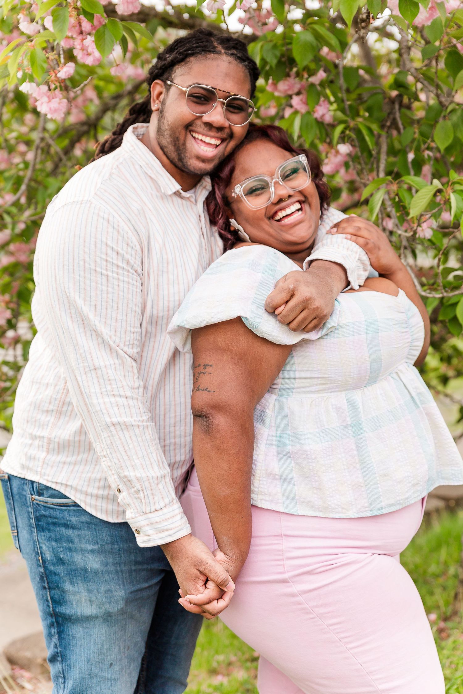 Couple embracing and laughing together under blooming spring trees.