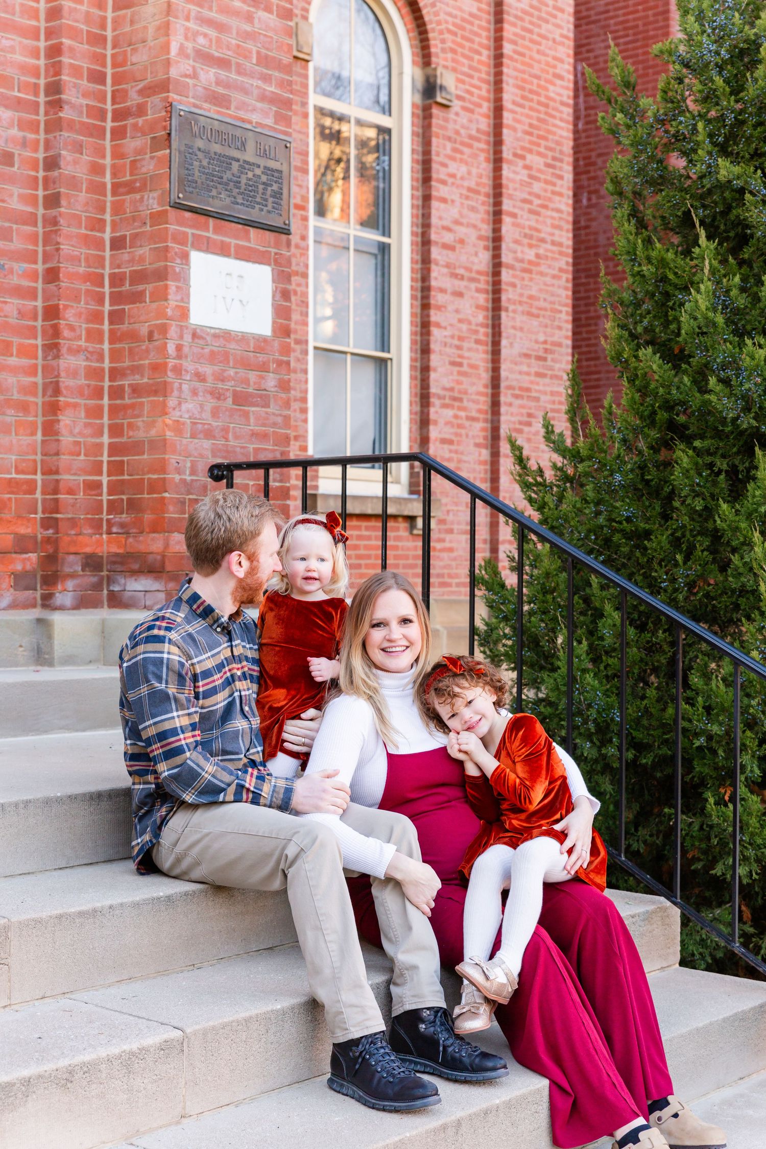 A family sits together on stone steps in front of a red brick building entrance.