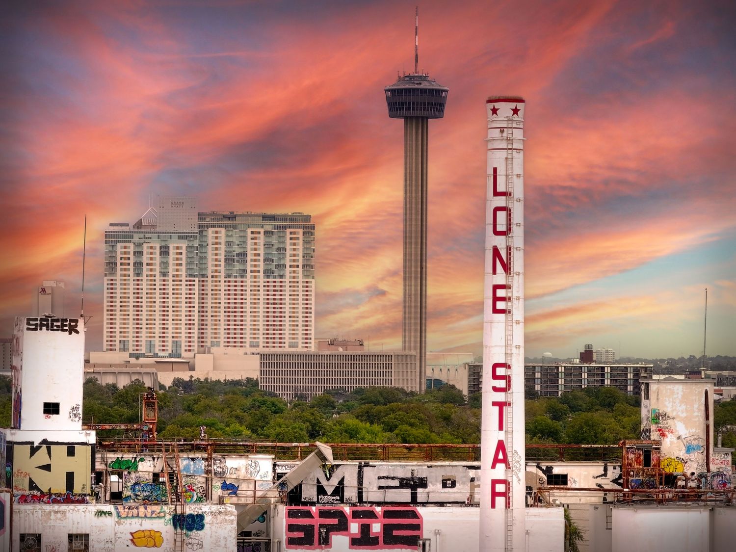 San Antonio skyline at sunset featuring the Tower of the Americas and abandoned Lone Star building with vibrant pink clouds.