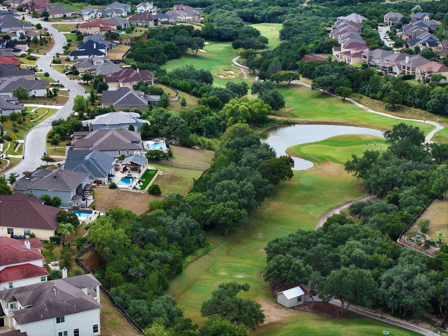 Aerial view of a suburban neighborhood surrounding a lush golf course with a pond and tree-lined fairways.