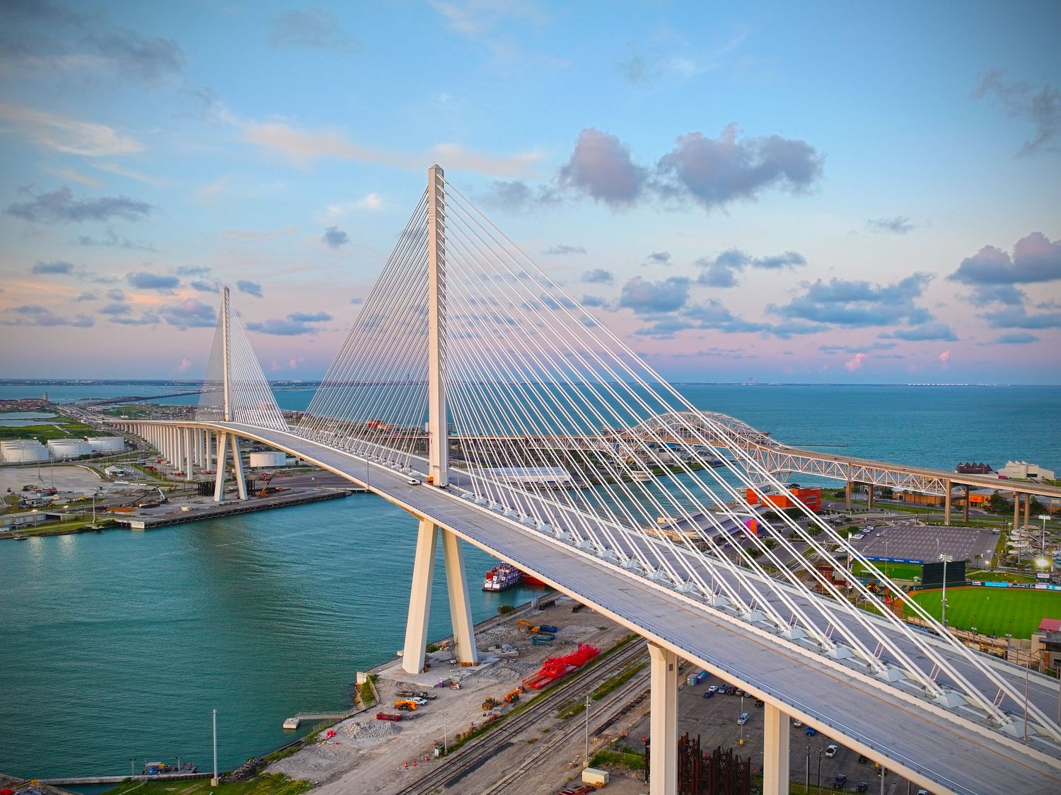 Aerial view of a modern cable-stayed bridge over Corpus Christi's blue harbor waters at sunset.