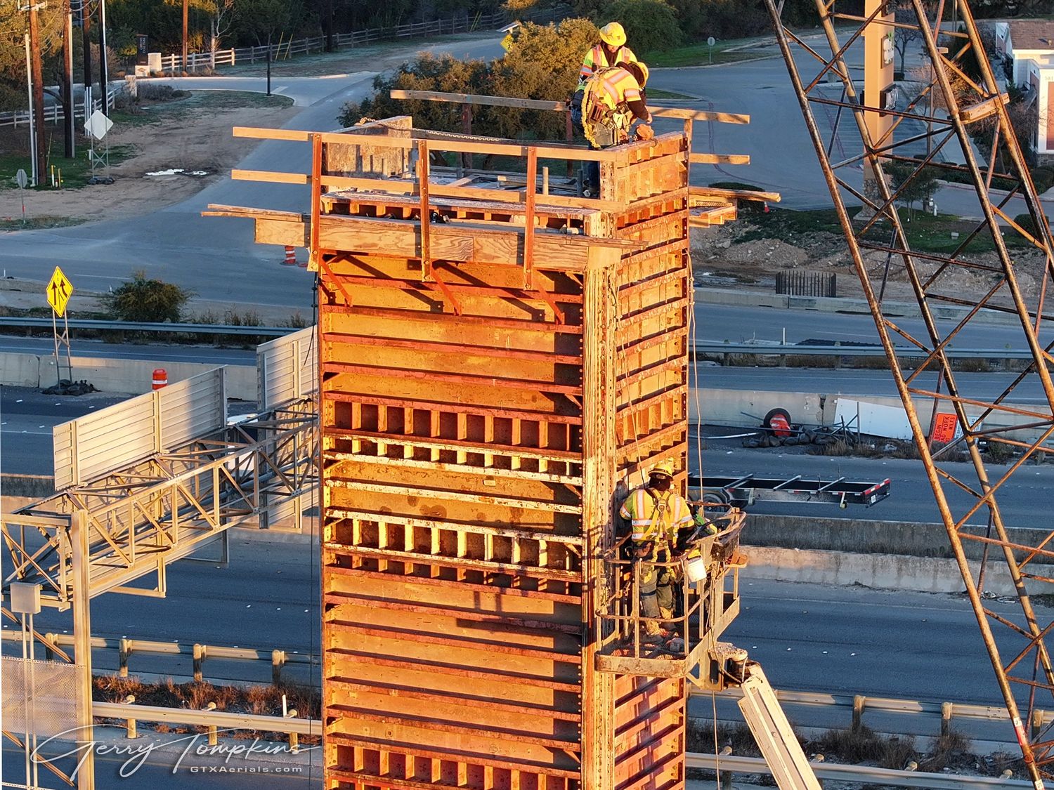 Workers atop a tall wooden concrete formwork tower at a construction site, photographed at golden hour.