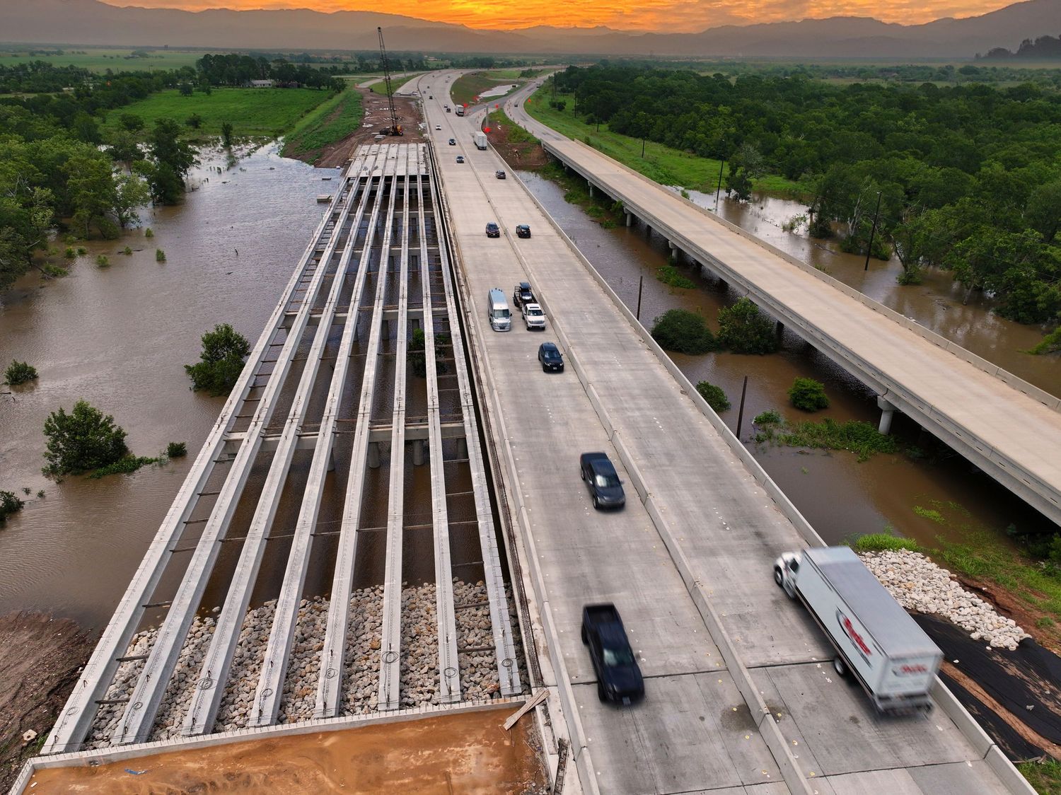 Aerial view of a highway interchange at sunset with cars driving on elevated roads above rising floodwaters.