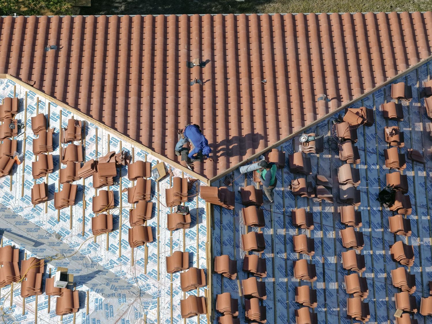 Aerial view of roofers installing terracotta clay roof tiles on a building under construction.