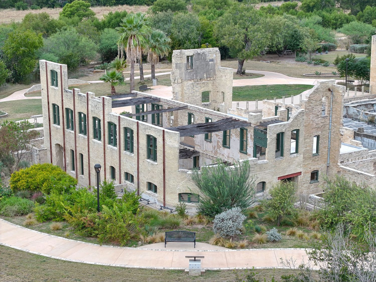 Aerial view of Hot Wells, historic stone ruins building surrounded by lush greenery and winding pathways in a park setting.
