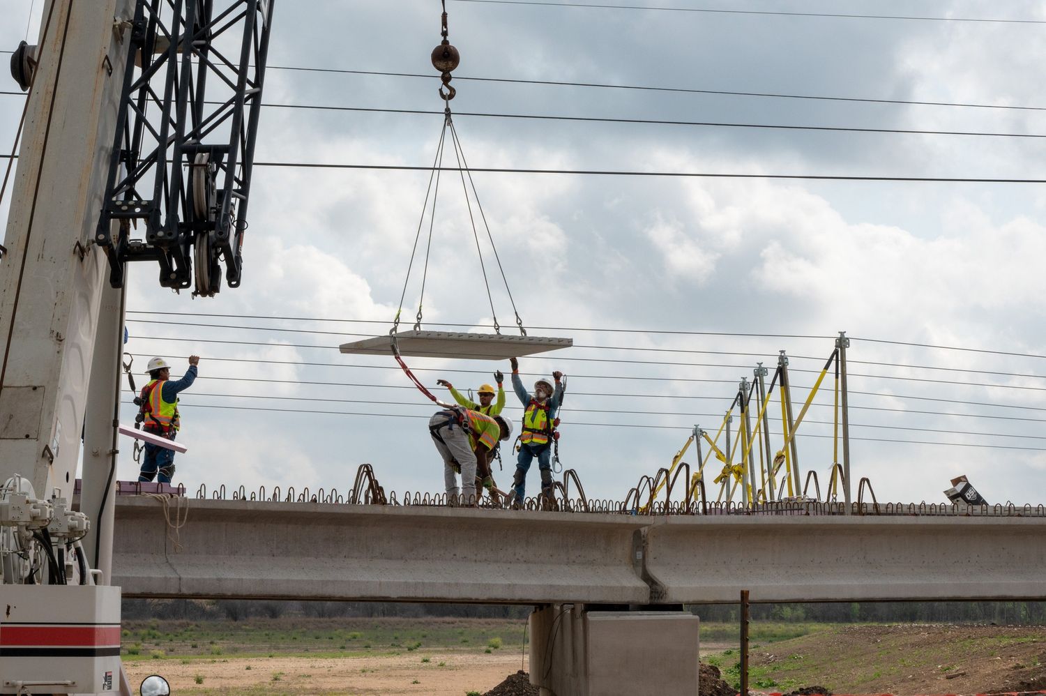 Construction workers use a crane to place deck panels onto a bridge at an active construction site.