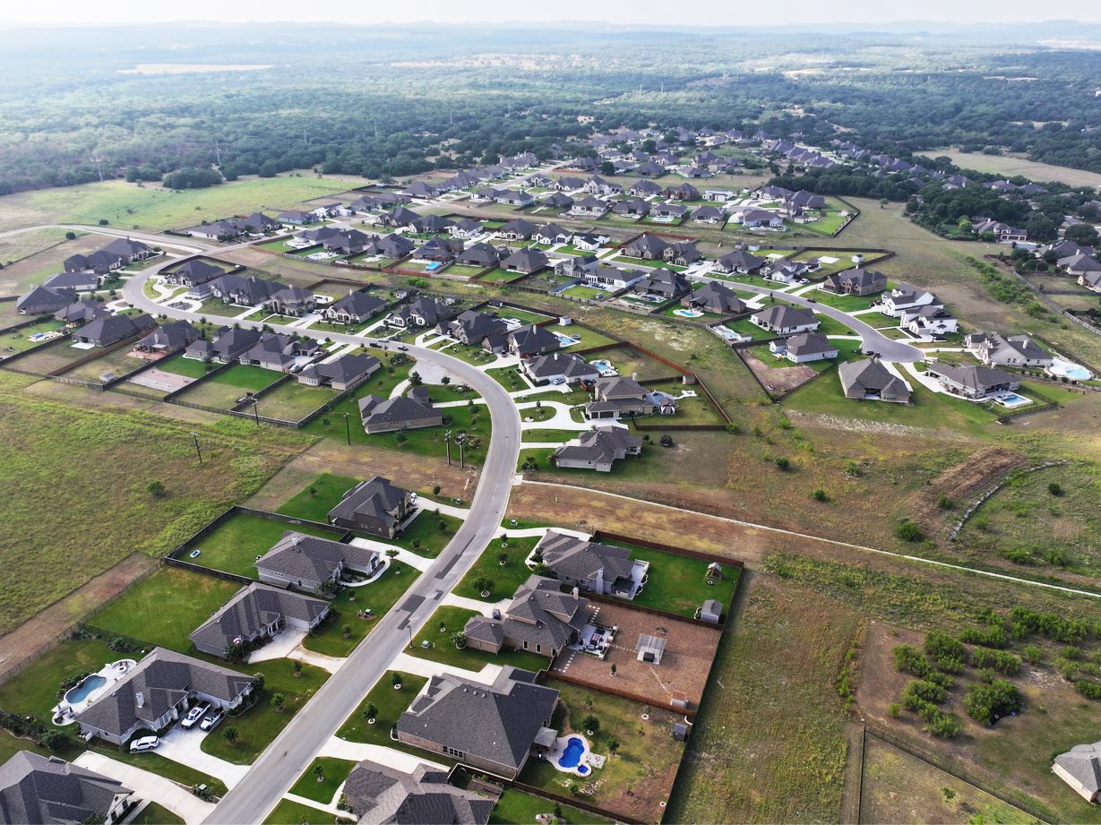 Aerial view of a suburban neighborhood with new homes, winding streets, and open lots in a rural setting.