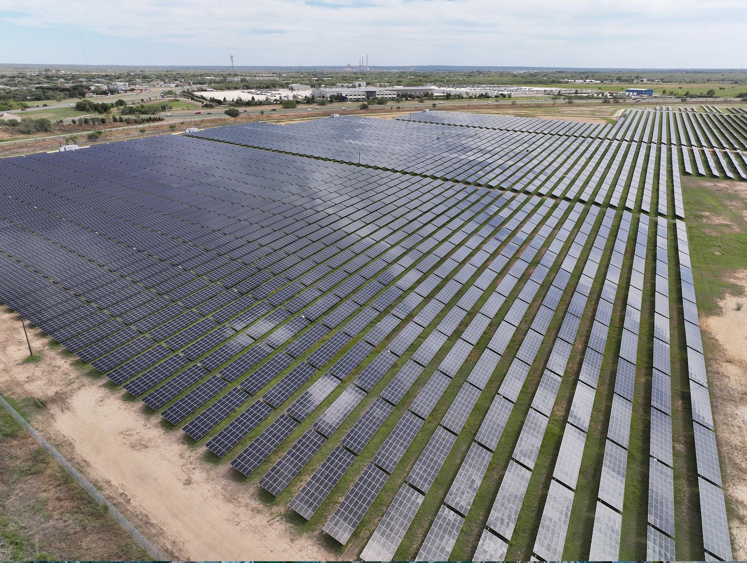 Aerial view of a large solar farm with rows of photovoltaic panels in a flat, open landscape under a clear sky.