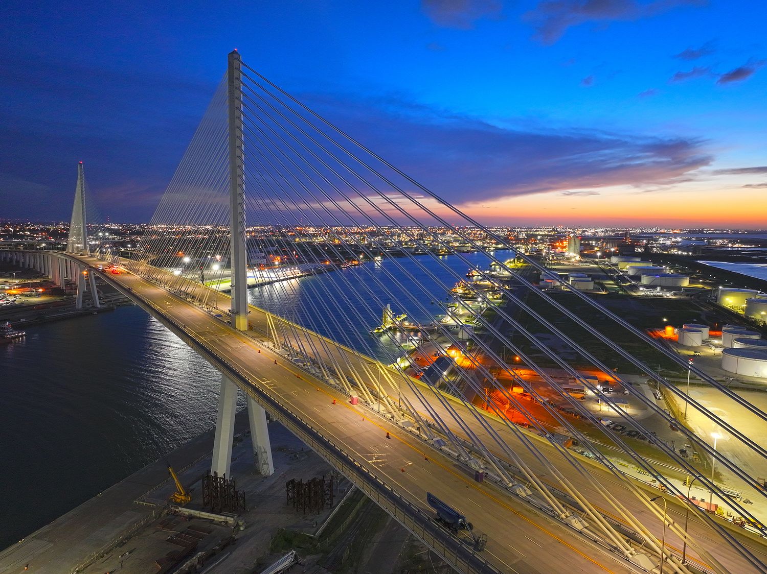 Aerial twilight view of the Corpus Christi harbor cable-stayed bridge with glowing city lights and colorful sunset sky.