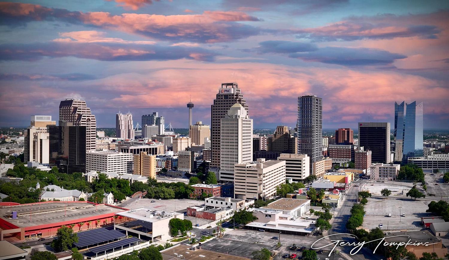 Aerial view of the San Antonio city skyline at sunset with dramatic pink and purple clouds over modern skyscrapers.