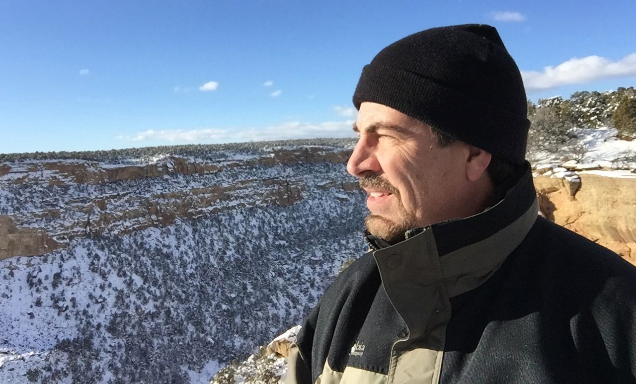 Man in black beanie and jacket gazing over snowy canyon landscape under clear blue winter sky.