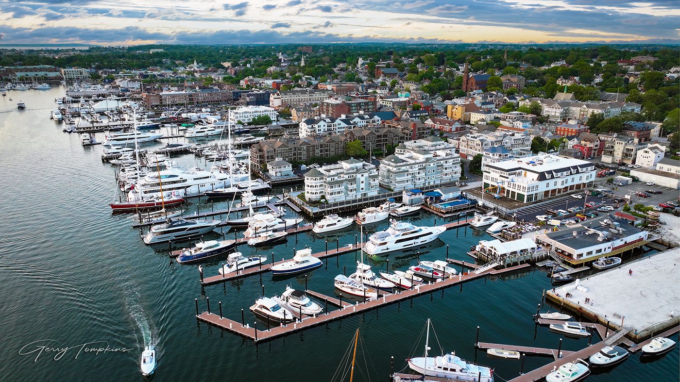 Aerial view of Newport harbor and marina with luxury yachts docked along piers in a scenic coastal New England town at dusk.