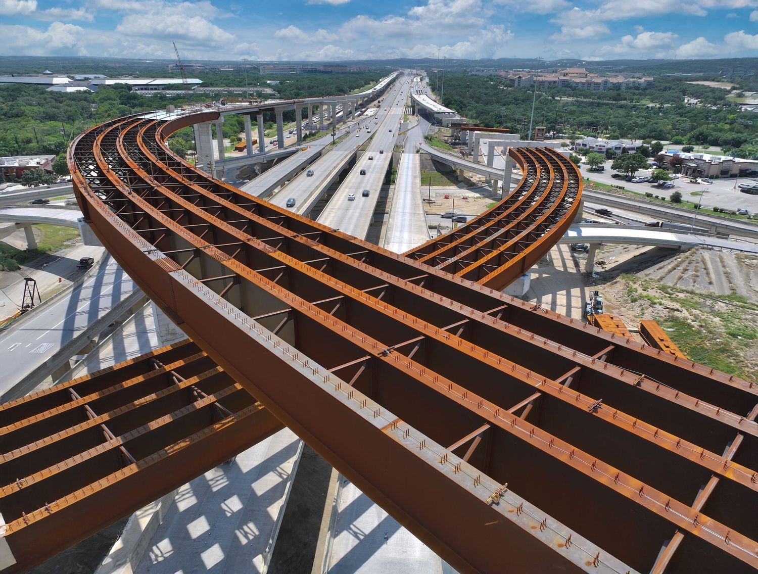 Aerial view of large curved steel girders for the I-10 & 1604 interchange fly-overs under construction with multiple elevated lanes.