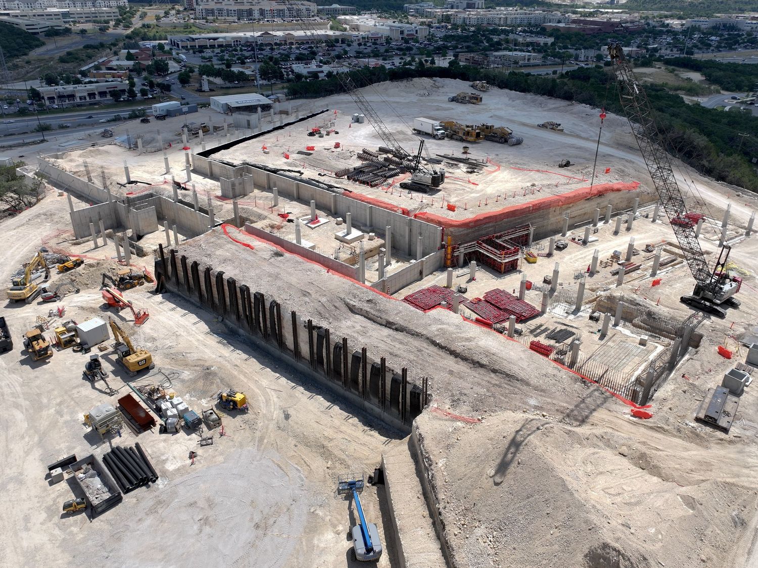 Aerial view of large commercial construction site with concrete foundations, steel columns, and heavy equipment in progress.