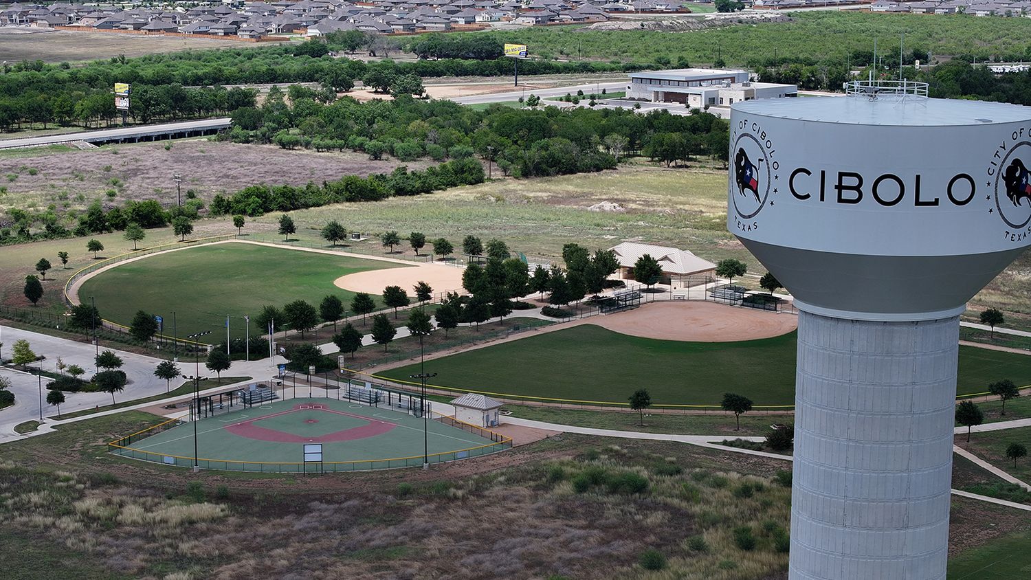 Aerial view of Cibolo, Texas water tower overlooking green sports fields and parks in a suburban landscape.