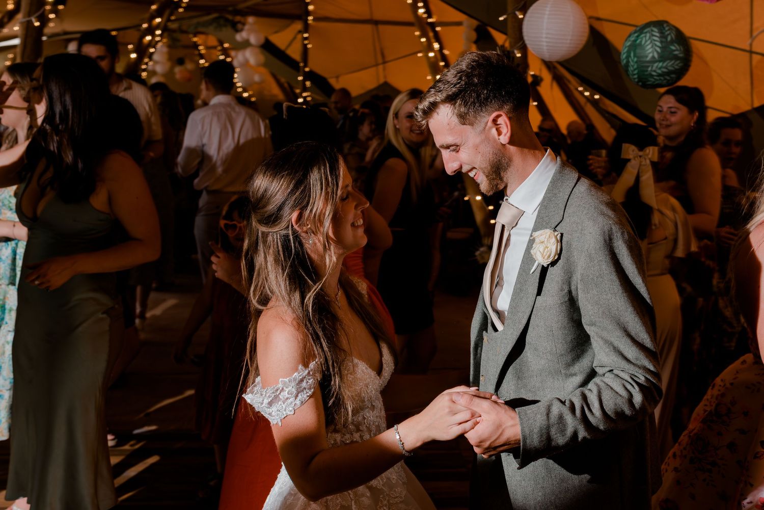 Couple dancing together at a wedding reception under warm lighting and string lights.