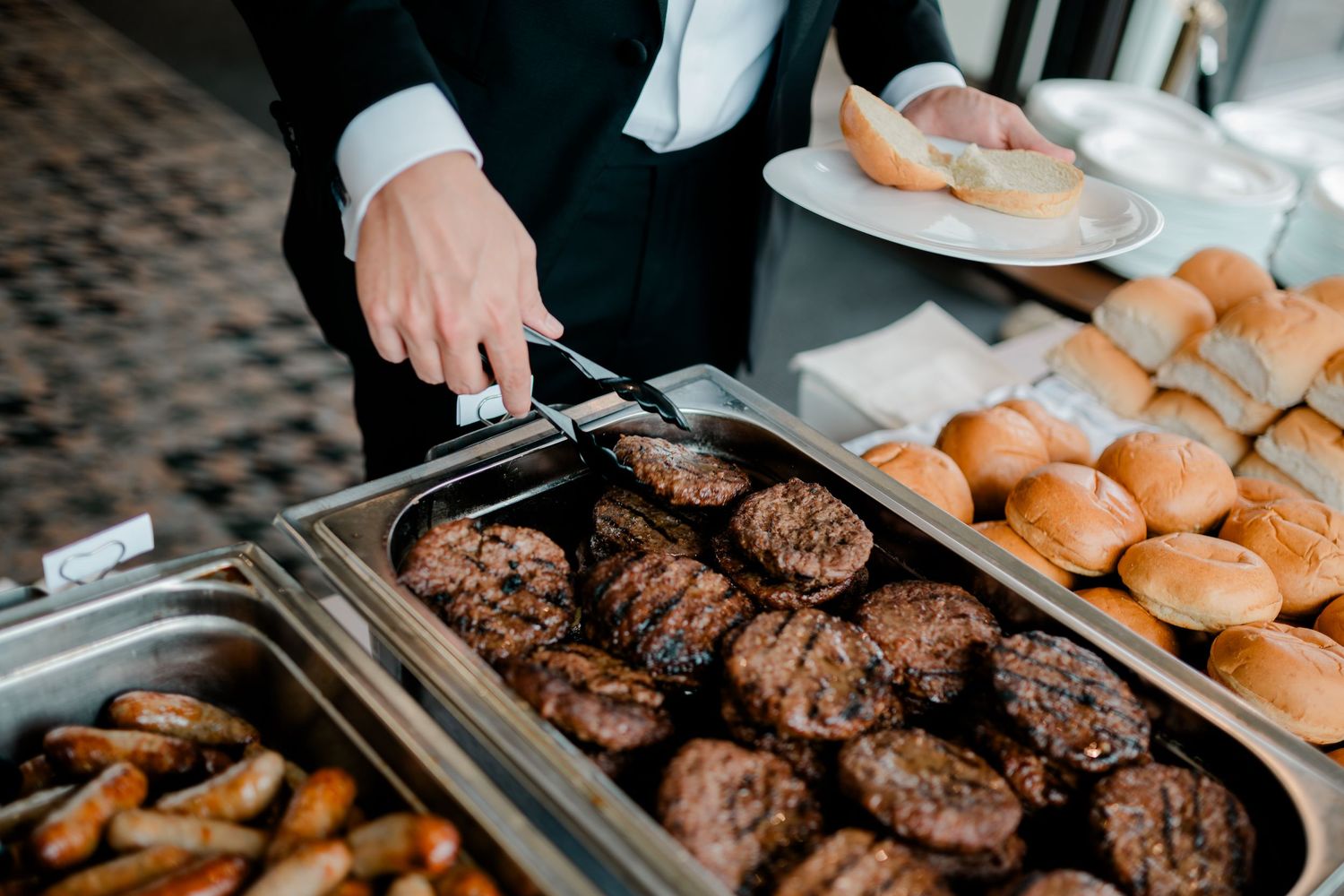 Grilled hamburger patties and buns being prepared on a metal serving tray.