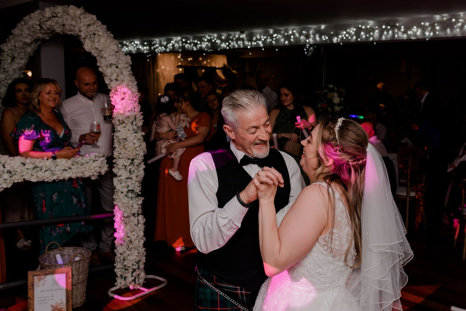 A couple shares a dance moment under twinkling lights at an evening wedding reception.