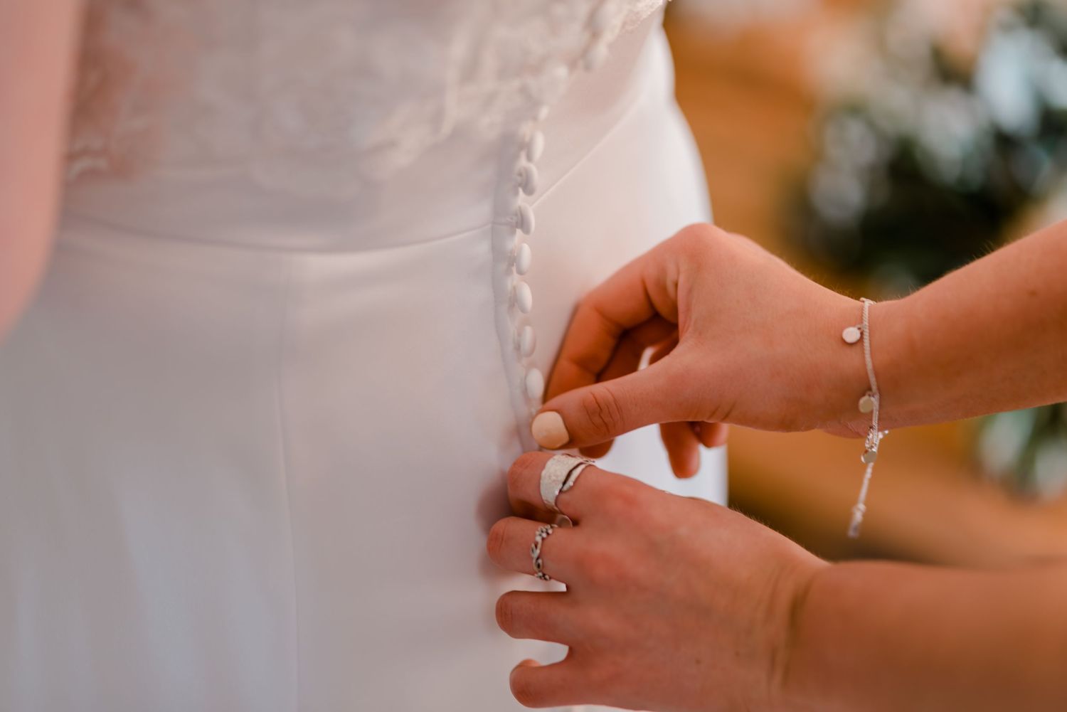 Close-up of hands buttoning delicate white wedding dress details.