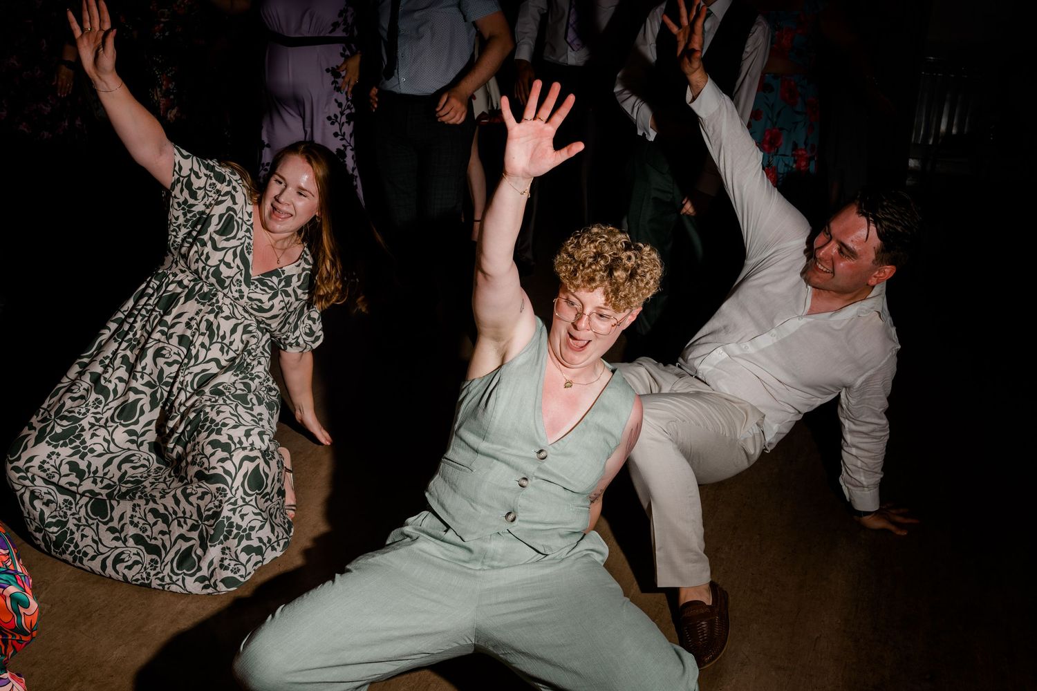 Lively dance floor scene with wedding guests dancing energetically in dark reception hall.