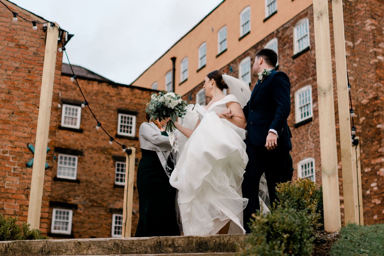 Bride and groom walking up stone steps outside a historic red brick mill wedding venue.