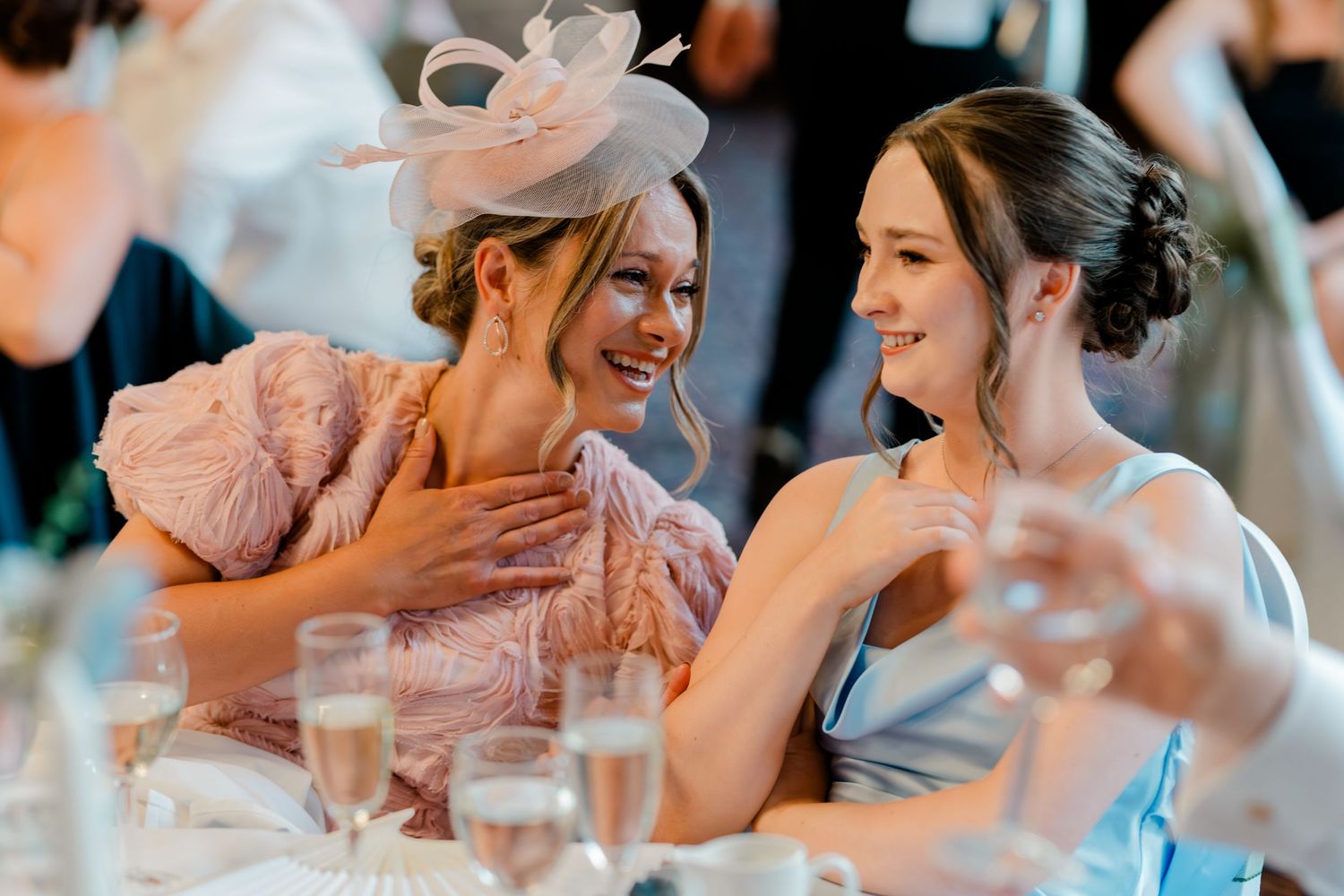 Two elegantly dressed female wedding guests laughing and chatting at the reception.