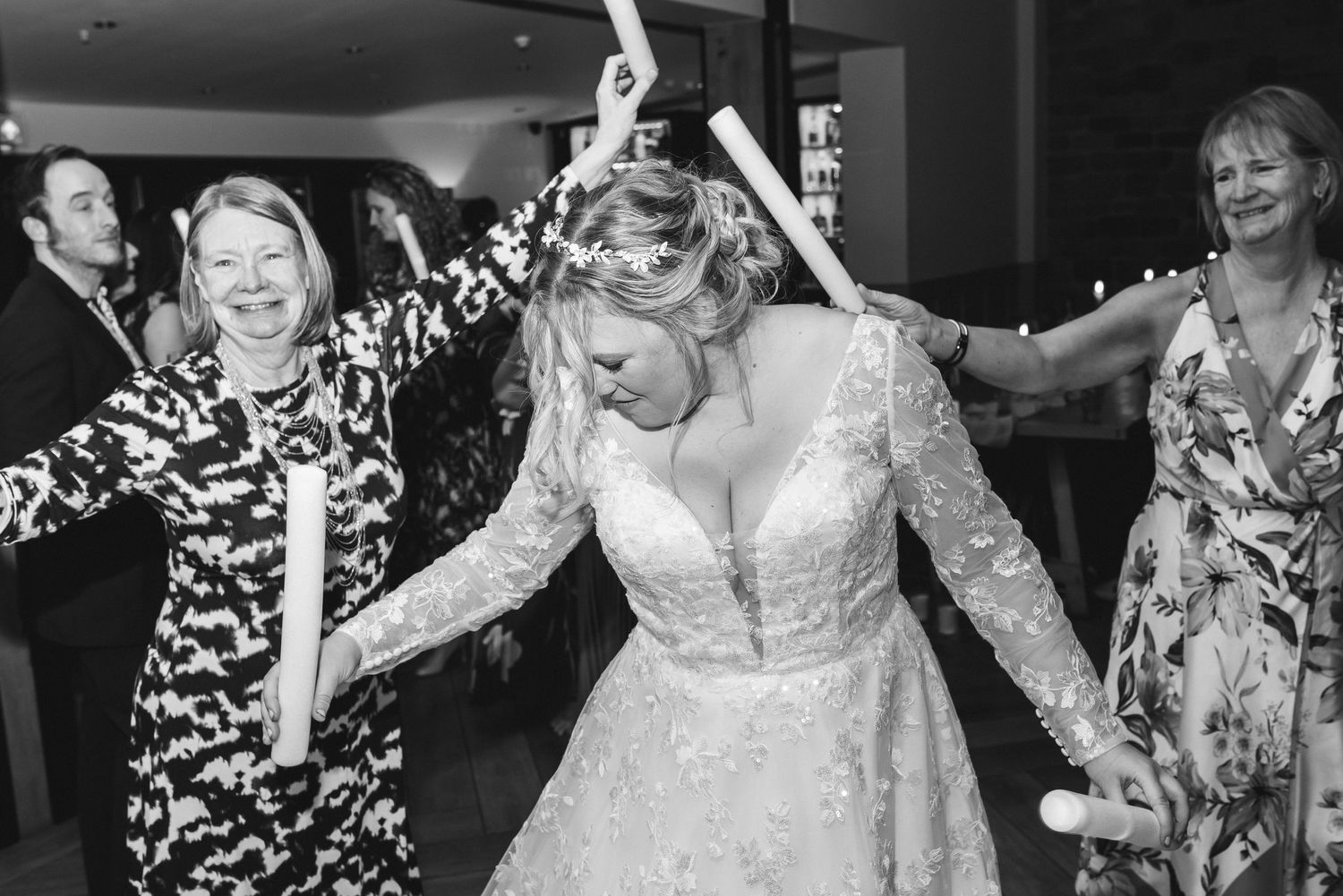 Black and white photo of joyful dance moments at a wedding reception with string lights overhead.