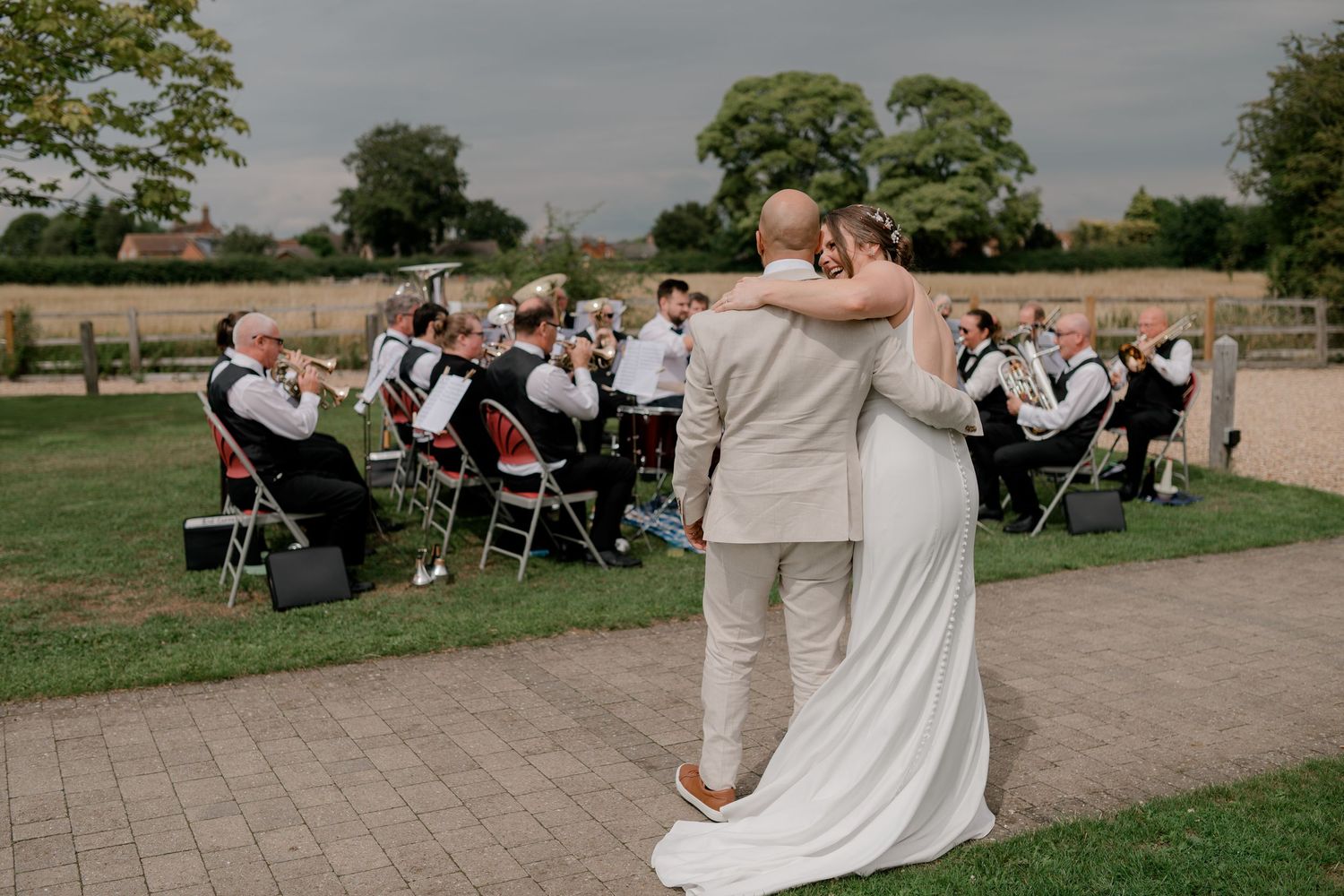 A couple embraces while a live band performs at an outdoor wedding ceremony.